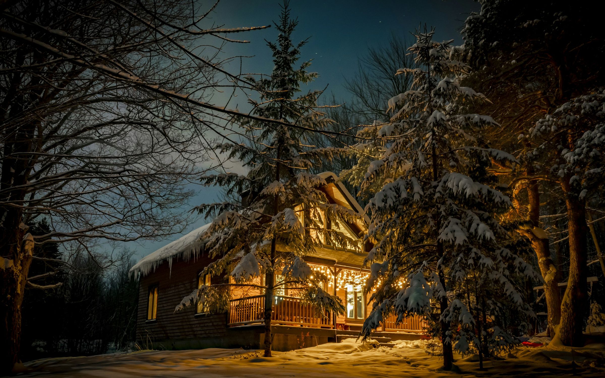 A home glowing warm in a snowy forest at night