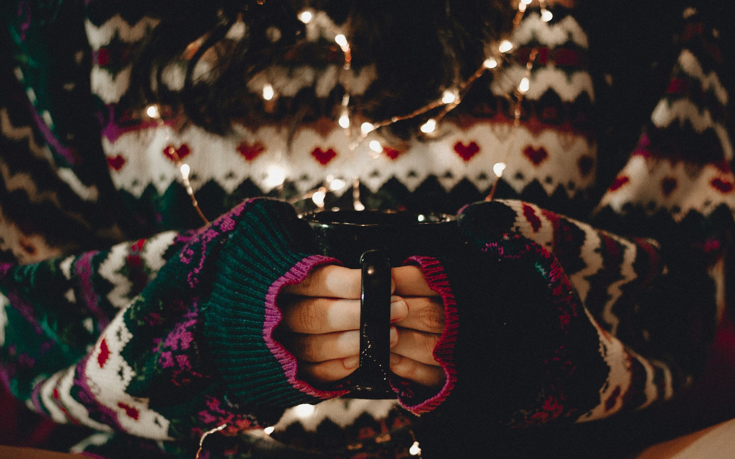 Hands wrapped around a warm mug in a cozy sweater