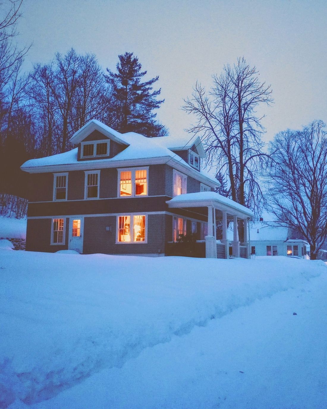 Snow-covered house with warm lights on at dusk